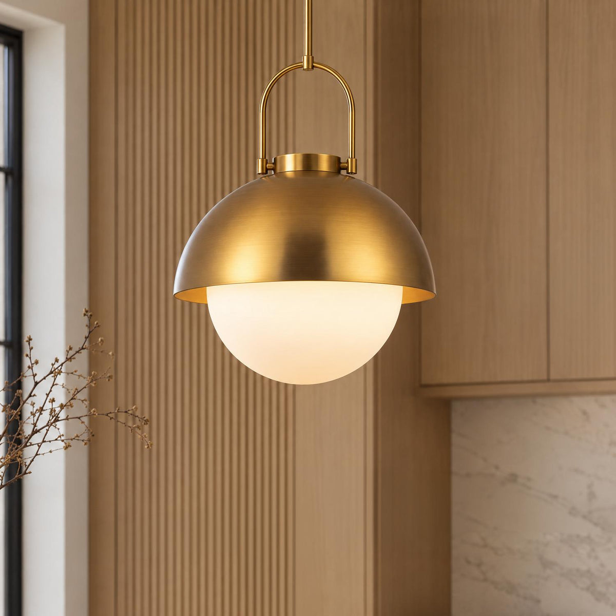 A contemporary kitchen featuring the Solene Pendant 16", Antique Brass and Opal Glass suspended beside fluted wood wall paneling, light wood cabinets, and marble backsplash.