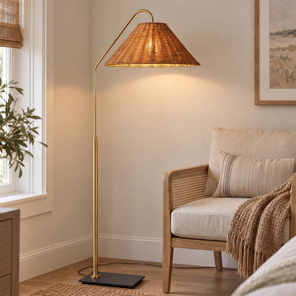 A coastal living room features the Fiona Floor Lamp, Aged Brass and Rattan standing beside a light wood cane armchair with a textured throw blanket.