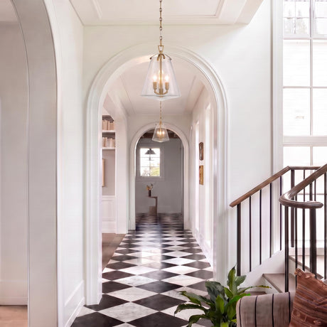 A transitional foyer with two brushed brass Addison Medium Pendants hanging along a coffered ceiling above black and white checkered marble floors and white arched doorways.
