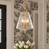 A transitional foyer features a brushed brass pendant light with a clear glass lantern shade suspended near black and white tree wallpaper and white tulips.