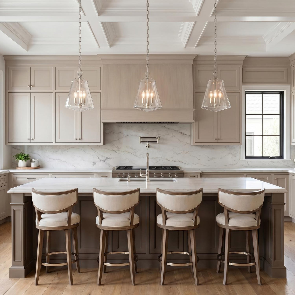 A transitional kitchen with three polished nickel lantern pendants hanging over a white marble island with taupe cabinets and a white coffered ceiling.