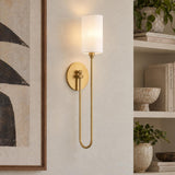 A transitional living room features the Briar Wall Sconce 24", Aged Brass with a white shade mounted on a textured wall beside built-in decorative shelves.