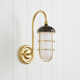 Sawyer Wall Sconce 13", Aged Brass and Distressed Bronze - A single wall sconce with a brass arm and bronze shade is mounted on a white wood panel wall.