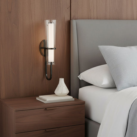 Clair 20" Sconce above a wooden nightstand with decorative items next to a bed with gray headboard and pillows.