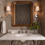 A transitional bathroom with two Magnolia Single Wall Sconce, Polished Nickel fixtures featuring white linen shades flanking a gold framed mirror over a white marble vanity.