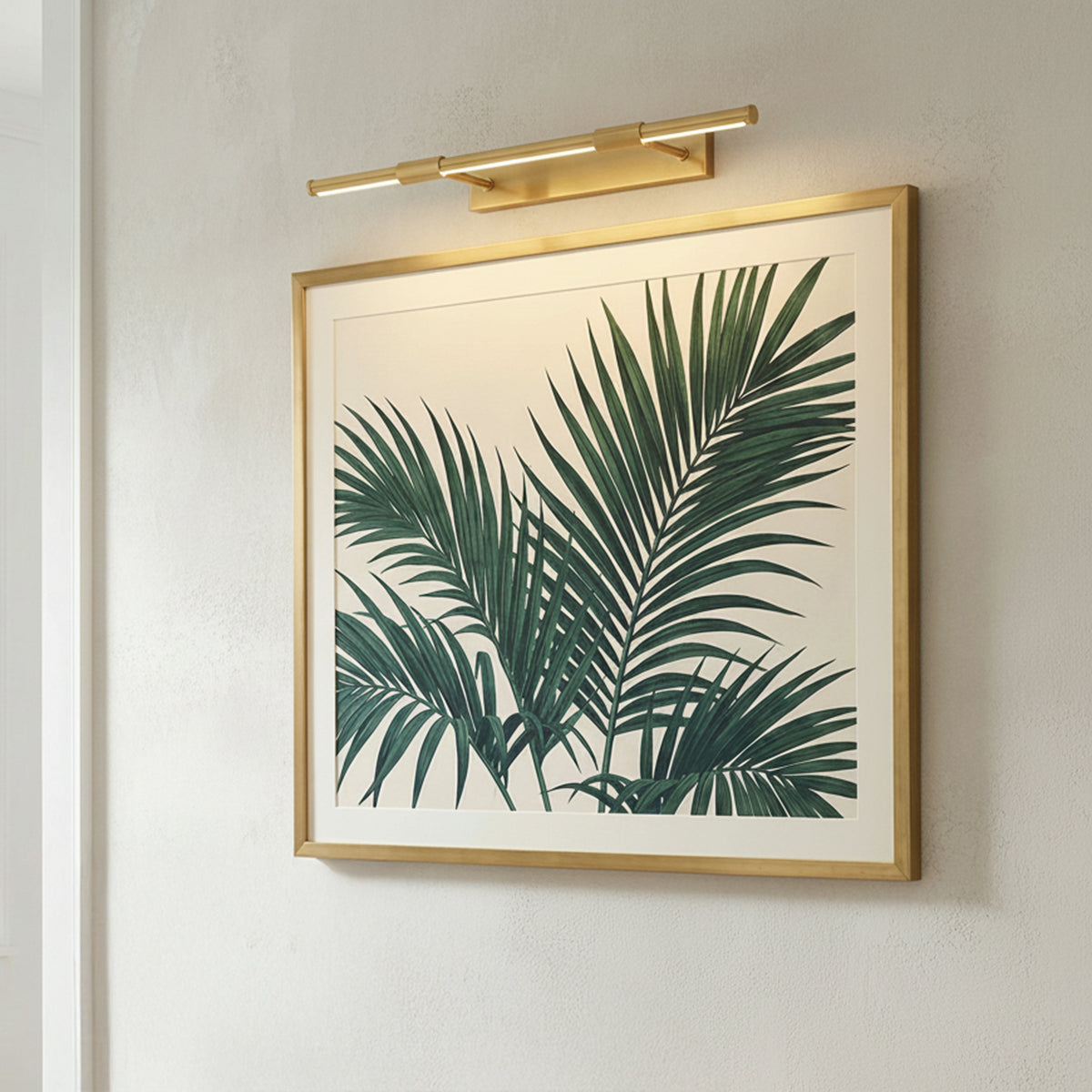 Ethan Extra Large LED Picture Light, Aged Brass linear Picture Light in a Modern Living Room with framed palm leaf artwork.