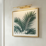 Ethan Extra Large LED Picture Light, Aged Brass linear Picture Light in a Modern Living Room with framed palm leaf artwork.