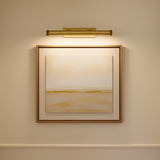 Abstract painting in a gold frame on a beige wall illuminated by the Graham Large 24.5" Picture Light in aged brass.