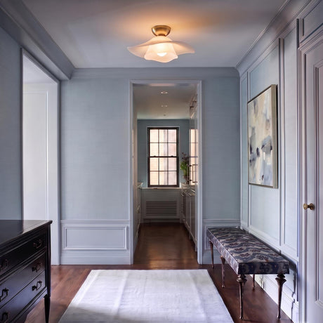 A transitional foyer with light blue paneled walls featuring an aged brass semi-flush mount light with an opal glass shade above dark hardwood floors.