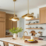 A Mid-Century kitchen with two Lola Pendant 22", Gold Leaf with Milk Glass suspended over a white marble island featuring light wood cabinets and marble backsplash.