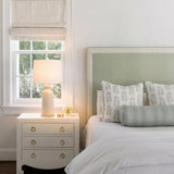 A traditional bedroom with the Bonnie Ceramic Table Lamp, Antique Ivory featuring a linen shade on a white nightstand beside a sage green headboard.
