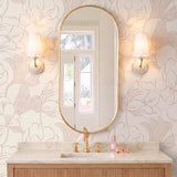 A transitional bathroom with two Bonnie Ceramic Wall Sconces in antique ivory and aged brass flanking an oval mirror above a marble vanity with floral wallpaper.