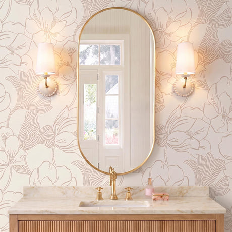 A transitional bathroom with two Bonnie Ceramic Wall Sconces in antique ivory and aged brass flanking an oval mirror above a marble vanity with floral wallpaper.