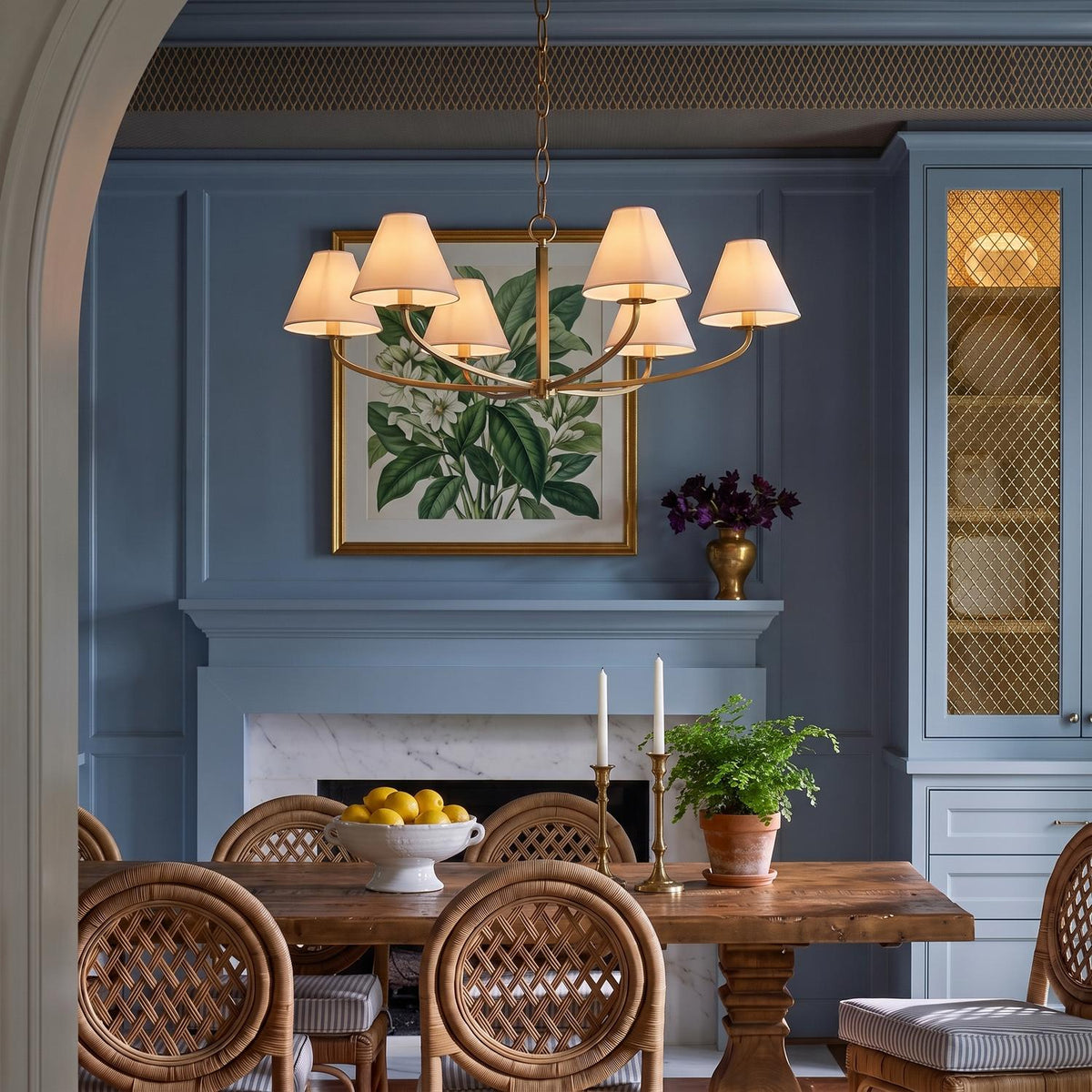 A transitional dining room features a Morgan 6 Light Chandelier 40 in Aged Brass over a wooden dining table surrounded by woven rattan chairs and blue paneled walls.