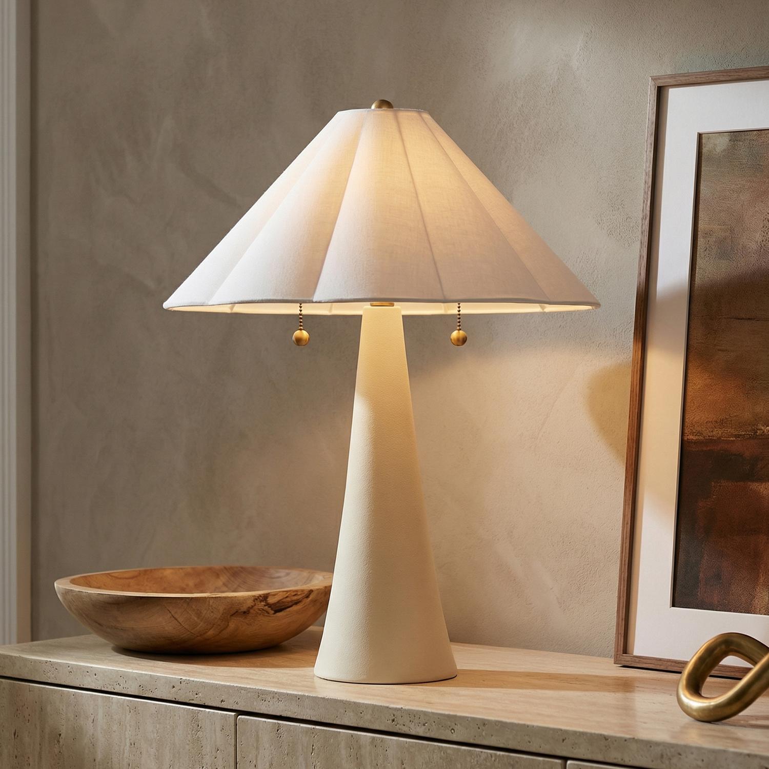 Liza Ceramic Table Lamp, Antique Ivory with Brass Accents scalloped Table Lamp in a Transitional Living Room with a travertine console.