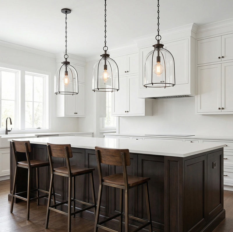 A transitional kitchen features three Lana Pendant 16", Old Bronze and Clear Glass pendants over a white quartz island with dark wood stools and white cabinets.