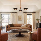 A transitional living room with the York 3 Light Chandelier in patina brass and soft black centered on a vaulted ceiling over a tan leather sofa.