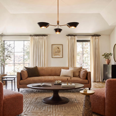 A transitional living room with the York 3 Light Chandelier in patina brass and soft black centered on a vaulted ceiling over a tan leather sofa.