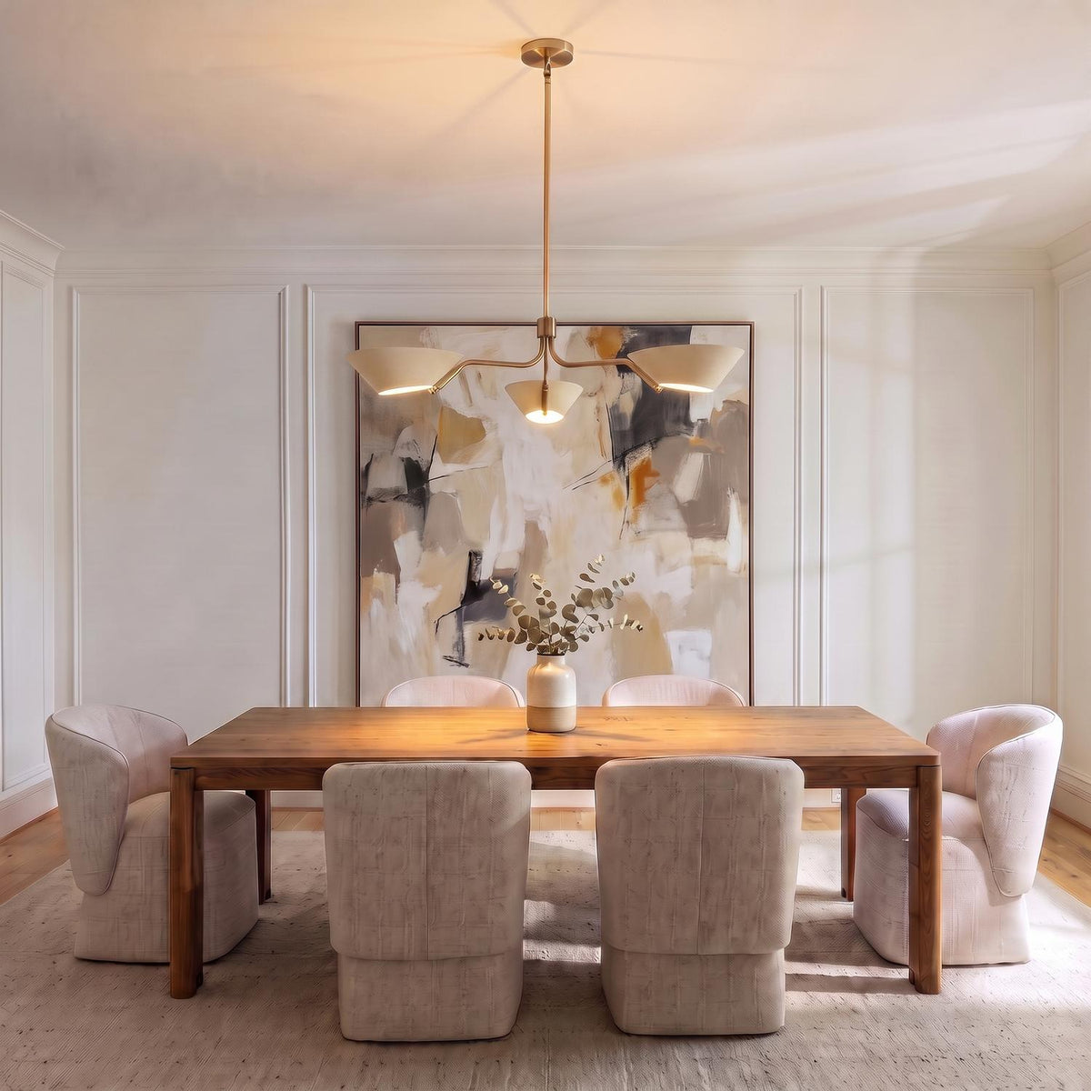 A transitional dining room with the York 3 Light Chandelier in patina brass and soft sand over a wood table and upholstered chairs with a large abstract painting.