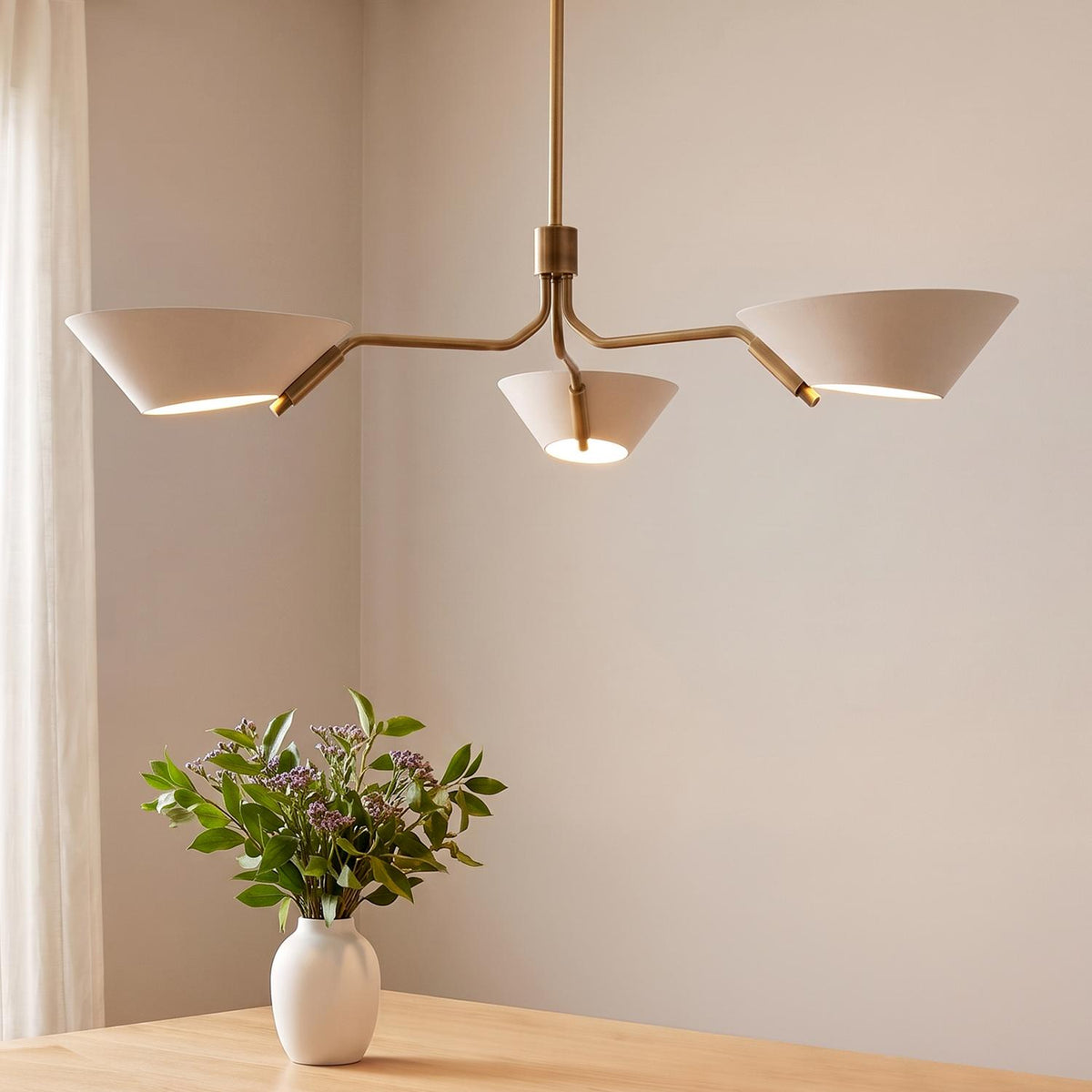 A mid-century dining room features the York 3 Light Chandelier 43", Patina Brass and Soft Sand hanging above a light wood table with a floral centerpiece.