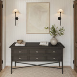 Two Scarlett 26" tall Wall Sconces, in Forged Iron finish, are above a dark wood console table with decorative items in a room with white paneled walls and wooden flooring.