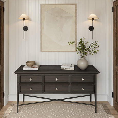 Two Scarlett 26" tall Wall Sconces, in Forged Iron finish, are above a dark wood console table with decorative items in a room with white paneled walls and wooden flooring.