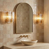 Aura Wall Sconce, Brass with clear linear glass Wall Sconce in a Modern Bathroom with a gold arched mirror and stone vessel sink.