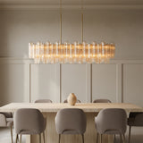 Grace Linear Chandelier 52, Brass with Topaz Glass - A long chandelier hangs over a dining table in a neutral-toned dining room.