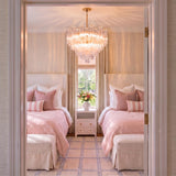 A transitional bedroom featuring the Grace 12 Light Chandelier 27", Brass with Clear Glass suspended above twin beds styled with soft pink bedding and upholstered headboards.