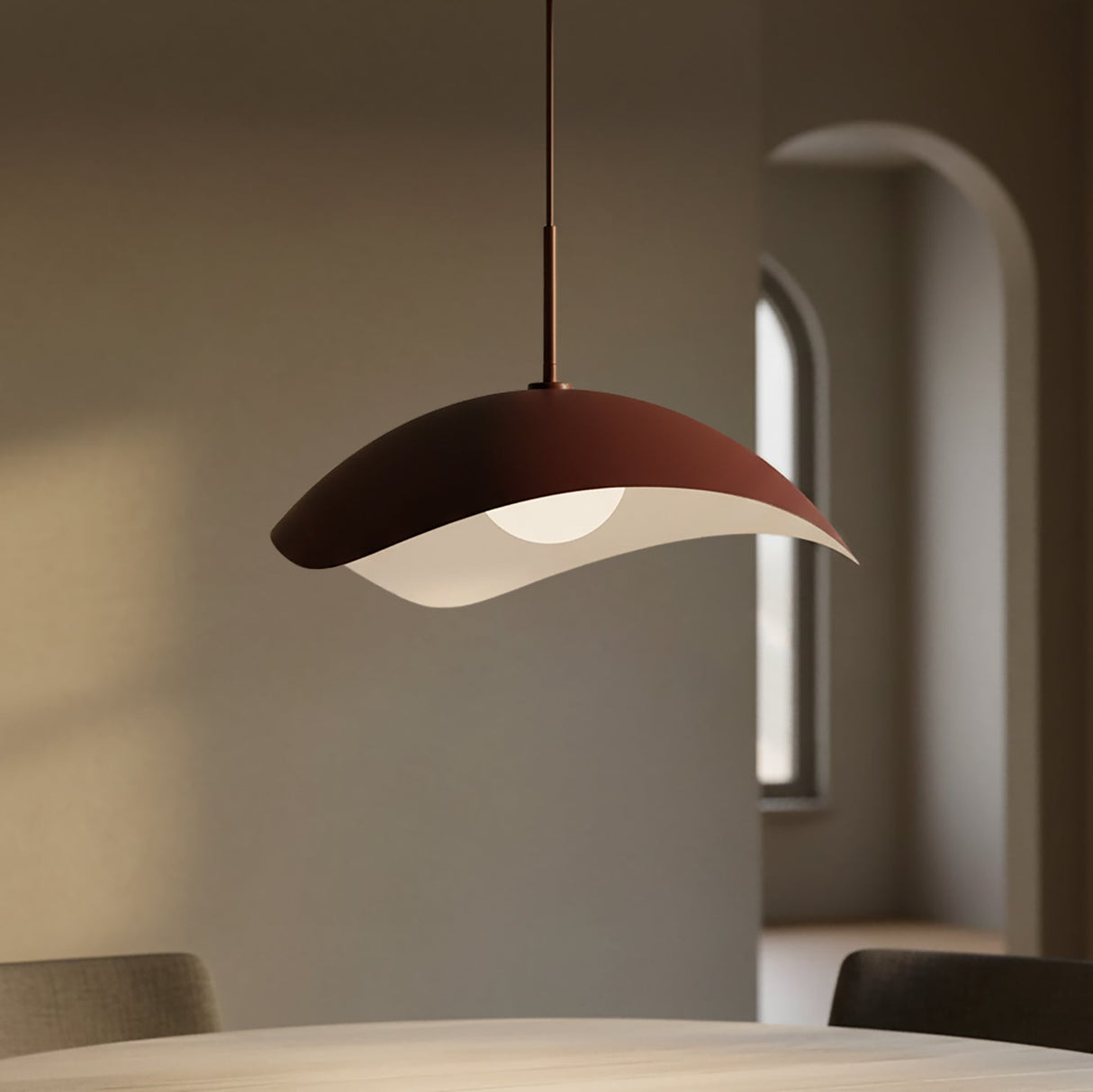 Modern maroon pendant light hanging above a table in a softly lit room.