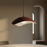 Modern maroon pendant light hanging above a table in a softly lit room.