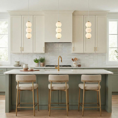 Aged Brass triple globe pendant in a Transitional Kitchen with a white marble island and gold bar stools.