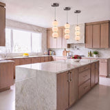 A contemporary kitchen with three brushed nickel and opal glass globe pendants suspended over a large white marble waterfall island surrounded by light wood cabinetry.