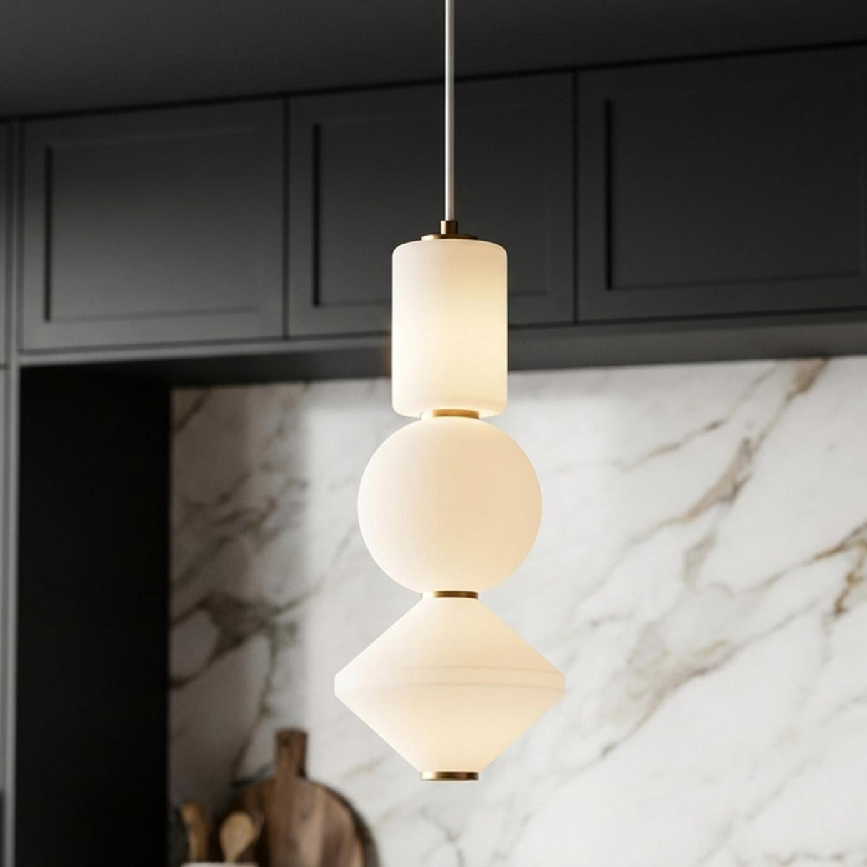 A contemporary kitchen with a Shai LED Pendant 8" in aged brass and opal glass over the island with a white marble backsplash and dark cabinets.