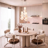 A contemporary dining area features Shai LED Pendant 8", Brushed Nickel and Opal Glass lights suspended above a round stone table with shearling chairs.
