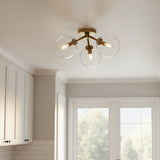 Gurt 3 Light Semi-Flush 18, Aged Brass - A three-light fixture with clear glass globes and aged brass finish is mounted on a white ceiling.