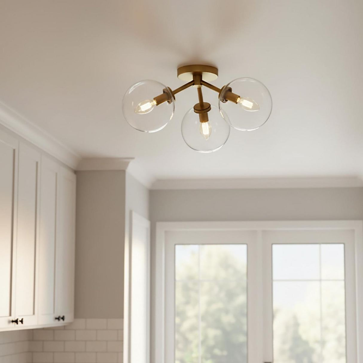 A transitional kitchen features the Gurt 3 Light Semi-Flush 18", Aged Brass flush mount along the ceiling beside white shaker cabinets and a white subway tile backsplash.