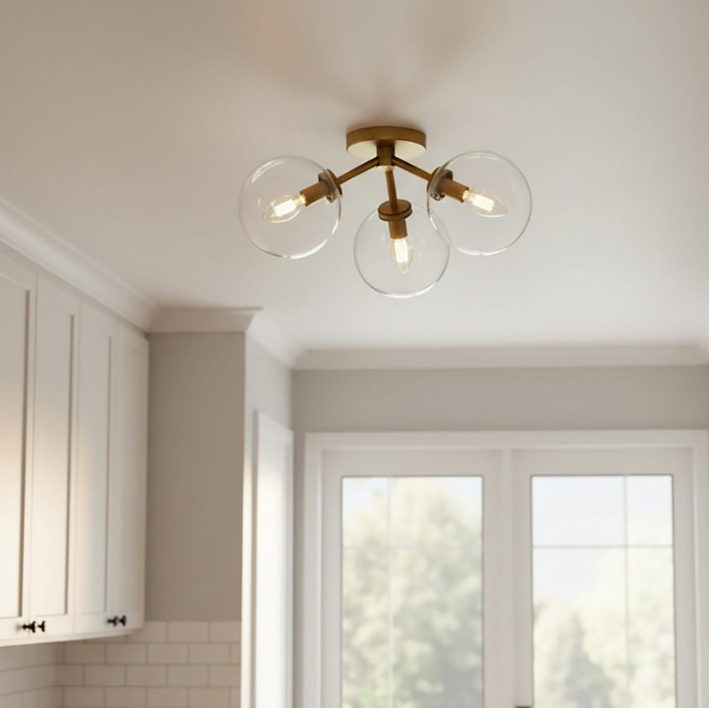 A transitional kitchen features the Gurt 3 Light Semi-Flush 18", Aged Brass flush mount along the ceiling beside white shaker cabinets and a white subway tile backsplash.