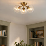 A transitional living room featuring the Gurt 3 Light Semi-Flush in aged brass with clear glass globes mounted above sage green built-in bookshelves.