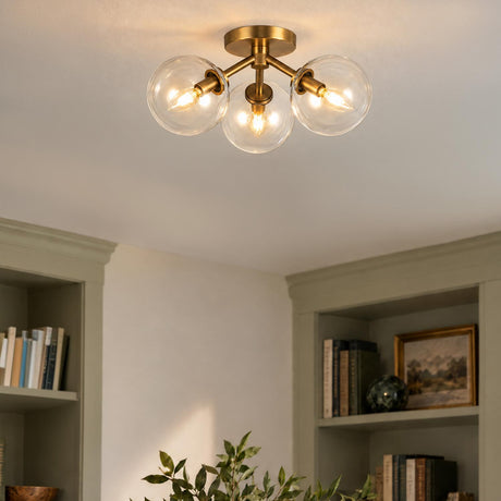 A transitional living room featuring the Gurt 3 Light Semi-Flush in aged brass with clear glass globes mounted above sage green built-in bookshelves.