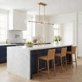 Aged Brass globe Linear Pendant in a Transitional Kitchen with white marble island & tan leather bar stools.