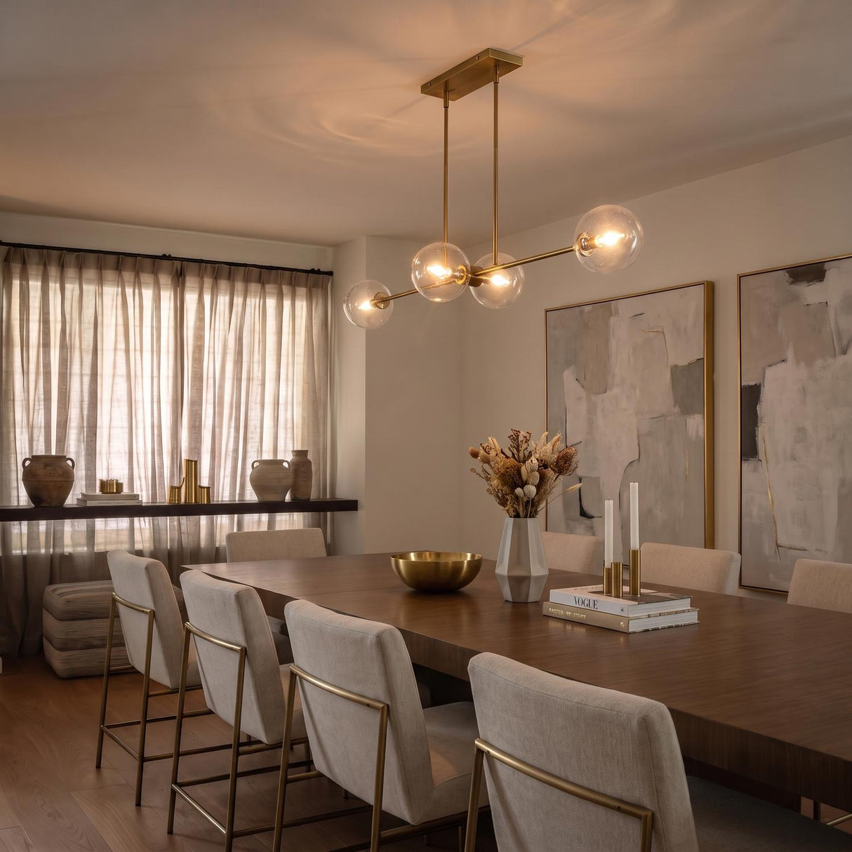 A transitional dining room with the Gurt 4 Light Linear Pendant 48 in aged brass featuring glass globes over a walnut dining table and cream chairs.