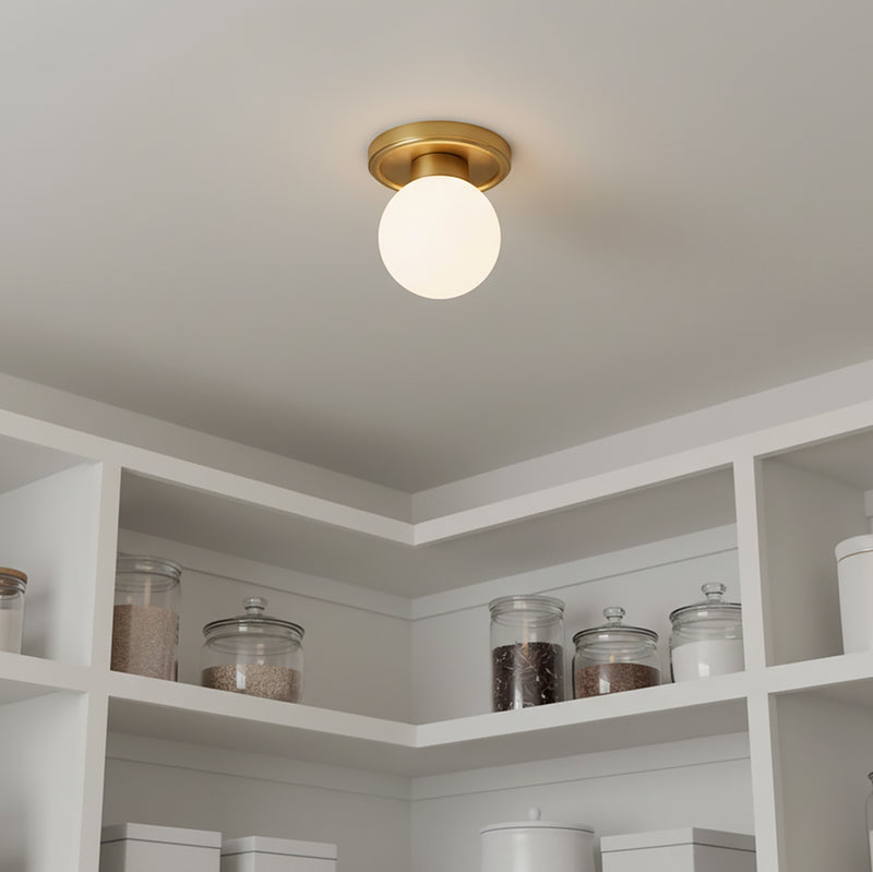 Tristen Flush Mount 6, Brushed Brass and Opal Glass - A ceiling fixture with a brass base and a white globe shade, set in a white kitchen.