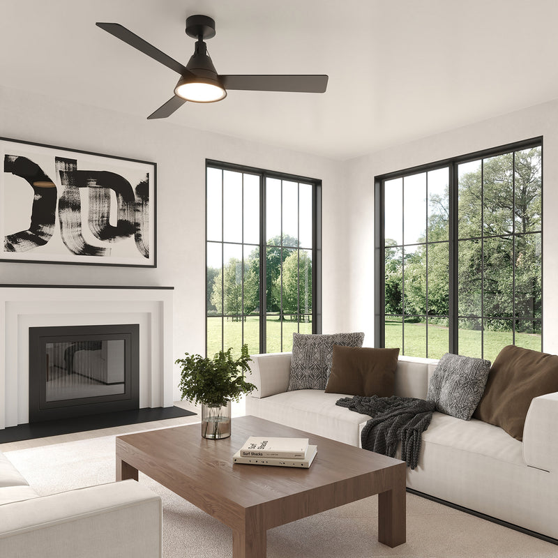 Monroe LED Ceiling Fan 54", Matte Black, shown in a contemporary living room with white walls,  large black frame windows, and modern art.