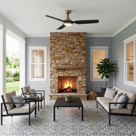 A modern farmhouse porch featuring the Hobbs LED Ceiling Fan in brushed brass and matte black mounted on the ceiling above patterned tiles and a stone fireplace.