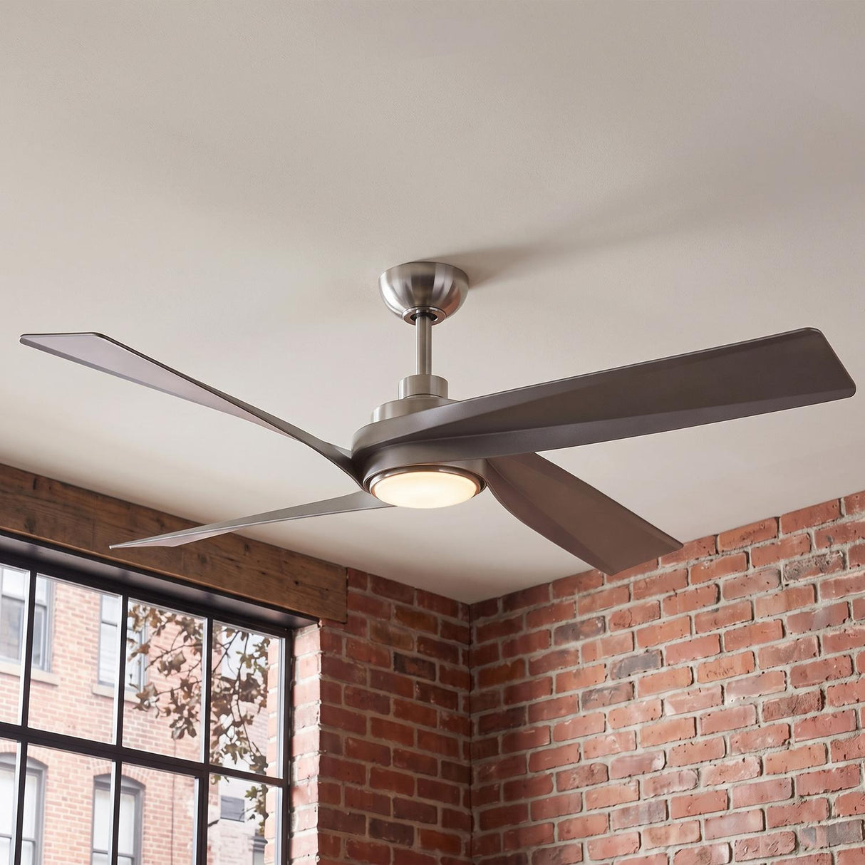 An industrial living room with a Largo LED Ceiling Fan 56-inch in brushed nickel centered on a white ceiling beside an exposed brick wall and large window.