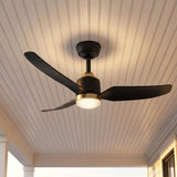 A modern farmhouse porch featuring the Kent LED Outdoor Ceiling Fan with Light in matte black and brushed brass glowing on a white beadboard ceiling at dusk.