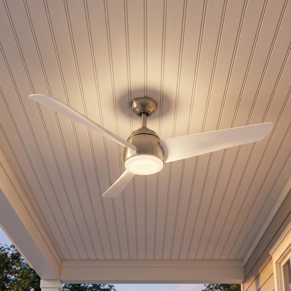 A modern porch featuring a Lorain LED Ceiling Fan 54", Brushed Nickel and White mounted on a white beadboard ceiling with horizontal siding and trees visible.