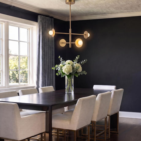 A contemporary dining room with the Sol LED Chandelier 23", Brushed Brass hanging over a dark wood table with white chairs and matte black walls.