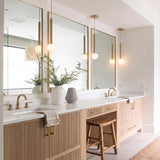 A modern bathroom featuring four brushed brass globe pendants with frosted glass shades hanging above a light wood slatted vanity and white quartz countertops.